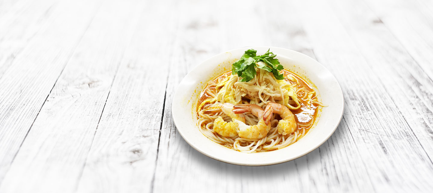 noodle-banner bowl of laksa on white wooden table